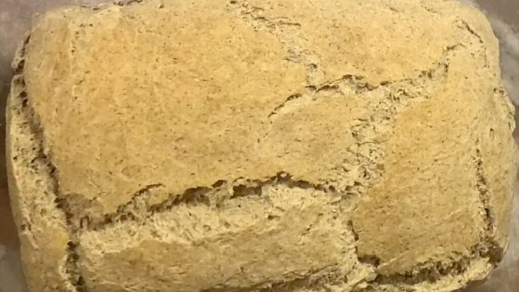 Pain au sarrasin au levain, rustique et moelleux, posé sur une planche en bois, avec une mie dense et légèrement humide.