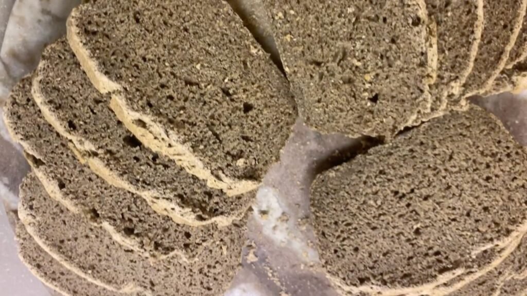 Pain au sarrasin au levain, rustique et moelleux, posé sur une planche en bois, avec une mie dense et légèrement humide.