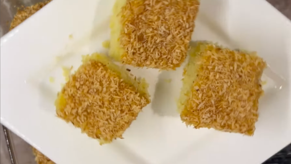 Bassboussa sans gluten au millet et à la noix de coco, nappée de miel et saupoudrée de coco dorée dans un moule.