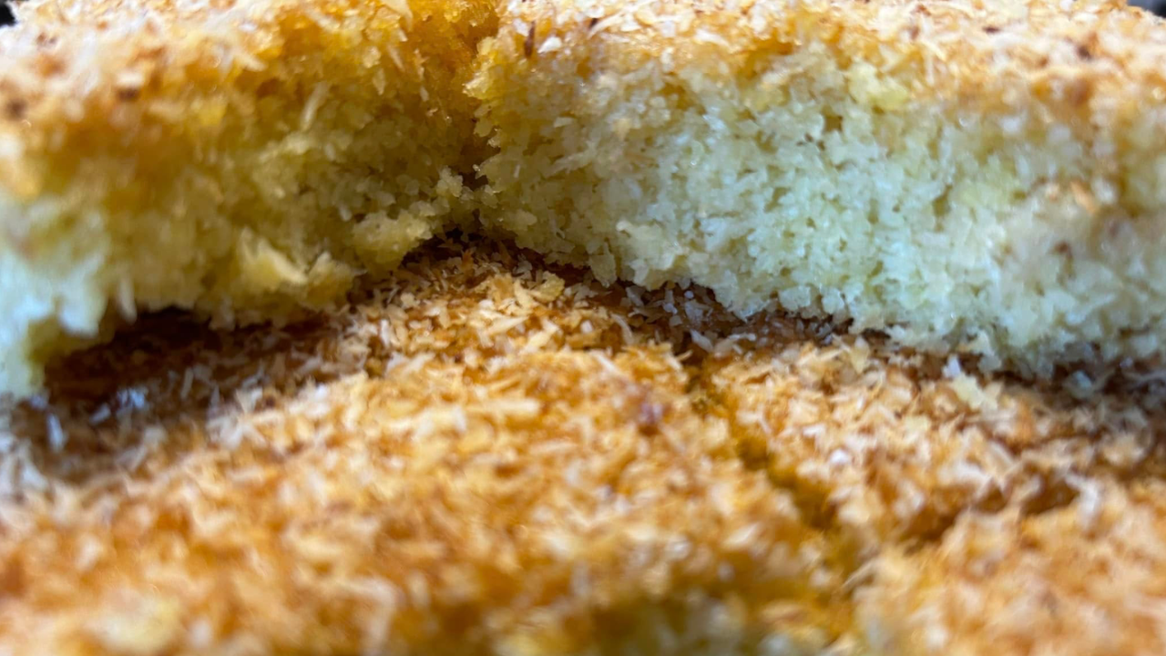 Bassboussa sans gluten au millet et à la noix de coco, nappée de miel et saupoudrée de coco dorée dans un moule.